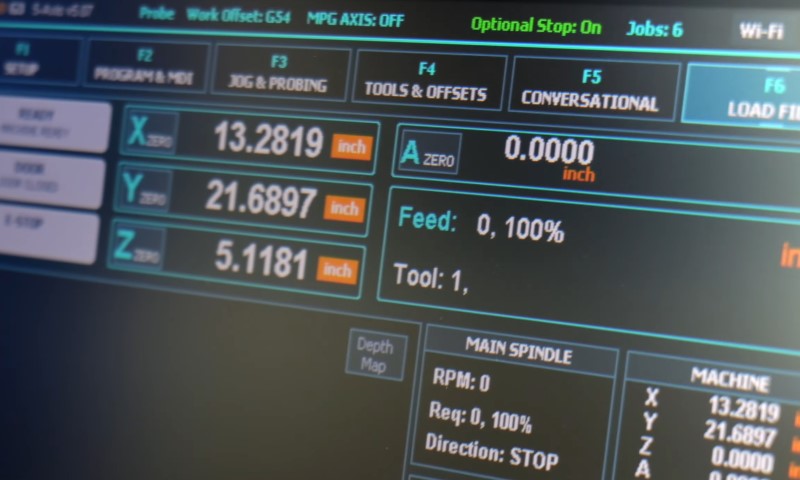 Close-up of a CNC machine's control screen displaying coordinates in inches, tool settings, and spindle status